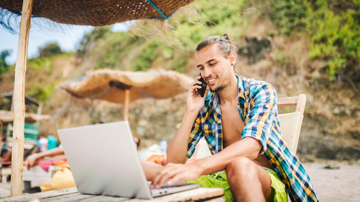 Digital nomad remote working on his laptop on the beach